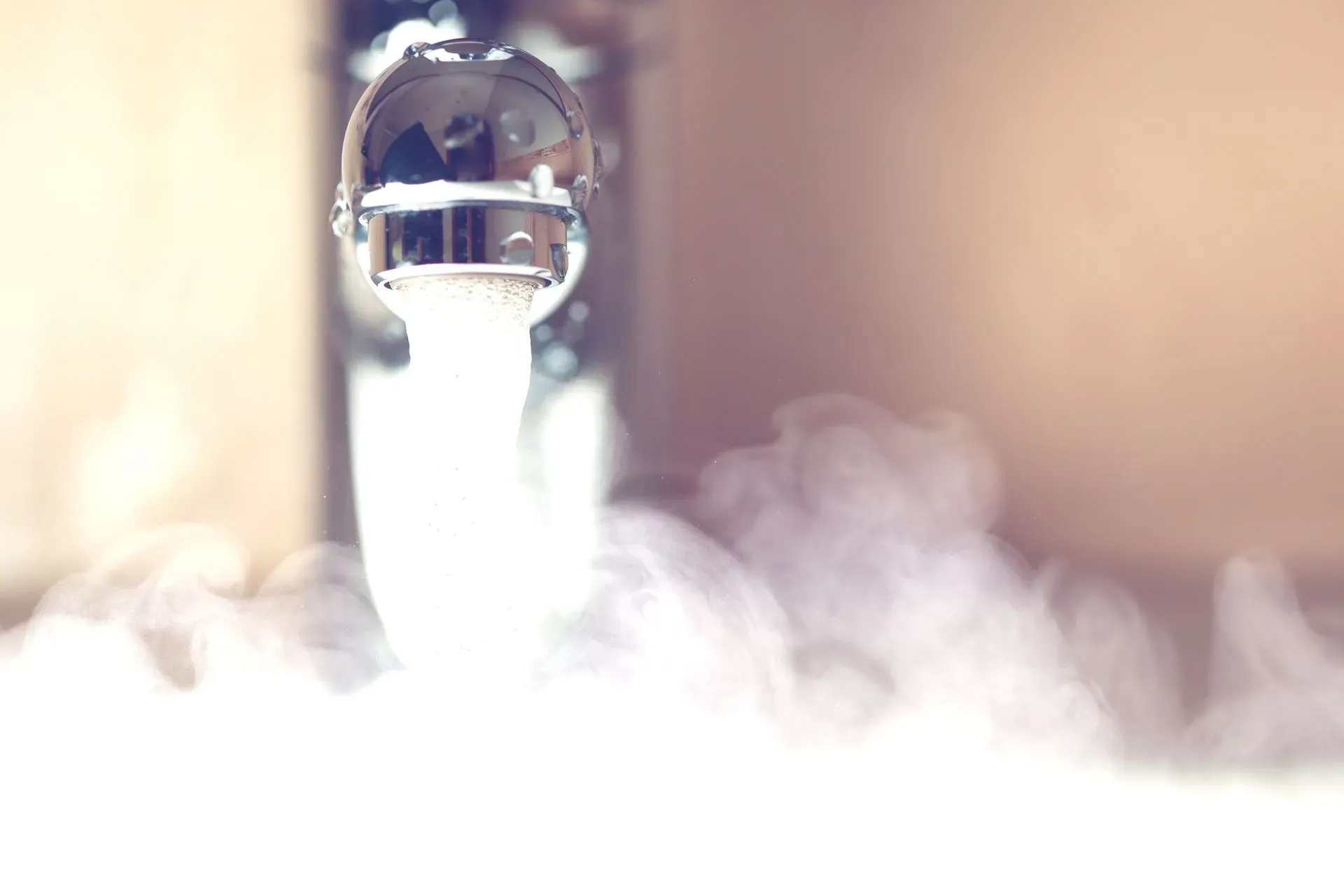 Close-up of a bathroom faucet running hot water with visible steam rising from the sink, highlighting hot water availability in a residential home.